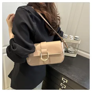 Chic beige patent leather baguette bag with gold horseshoe buckle on model's shoulder