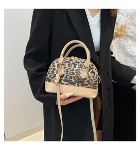 Detailed view of leopard print shell bag with beige leather trim held by a model