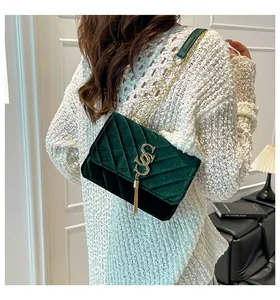 Détail du sac bandoulière en velours vert foncé avec matelassage en V et pompon doré