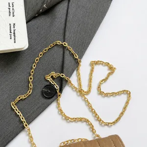 Detail of golden metal chain strap on a brown quilted velvet bag with gray fabric background