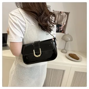 Detail of a black patent leather underarm bag with a gold horseshoe buckle and flap