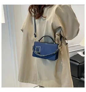 Detail of navy blue crossbody bag with metallic chain and geometric buckle on trench coat