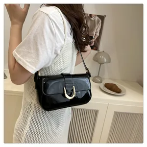 Detail of black patent leather shoulder bag with golden horseshoe buckle on a white dress