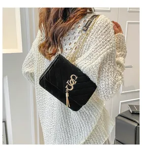 Détail du sac bandoulière en velours noir avec logo doré et pompon sur pull blanc