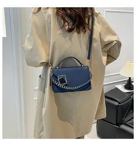 Close-up of navy blue rectangular shoulder bag with woven chain and gold metal buckle