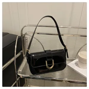 Detail of glossy black patent leather bag with gold horseshoe buckle on metal rack