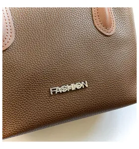 Close-up of brown lychee grain leather crossbody bag with silver FASHION logo hardware