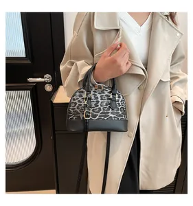 Detail of leopard print shell bag with gold hardware and black leather handle trim