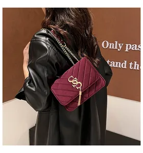 Détails du sac à bandoulière en velours bordeaux avec logo doré et chaîne à pompon