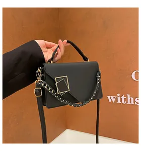 Detail of black leather crossbody bag featuring geometric gold buckle and chain strap