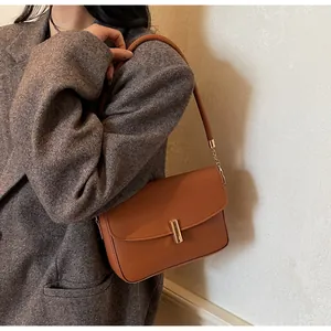 Detail of caramel leather shoulder bag with gold metal clasp on gray coat model