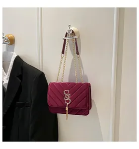 Détail du sac bandoulière en velours bordeaux avec surpiqûres en V et pompon argenté