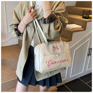 Detail of cream patent shoulder bag with pink ribbon bow and letter embroidery