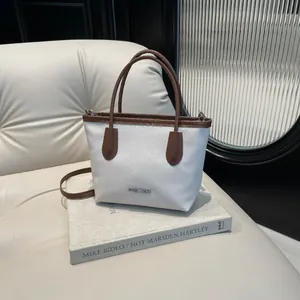 Minimalist white leather bucket bag with brown handles and fashion logo on book