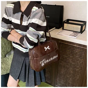 Detail of glossy brown patent leather shoulder bag with white bow and lettering