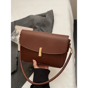 Classic dark brown leather rectangular crossbody bag with golden clasp on grey blazer