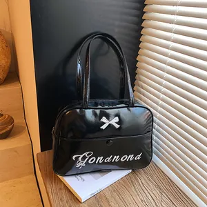 Glossy black patent leather shoulder bag with white bow and embroidery on a wooden surface