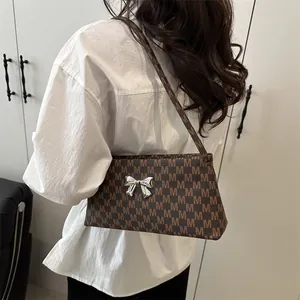 Brown monogram shoulder bag with a silver bow ornament shown in a lifestyle pose