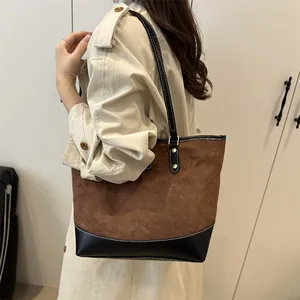 Braune gesteppte Wildleder-Tote-Bag mit schwarzem Lederbesatz an der Schulter eines Models