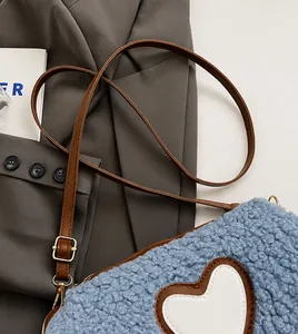 Detail of blue plush crossbody bag featuring heart patch and adjustable brown strap