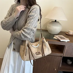 Sac hobo beige minimaliste avec chaîne en perles et pompon présenté dans un cadre chic