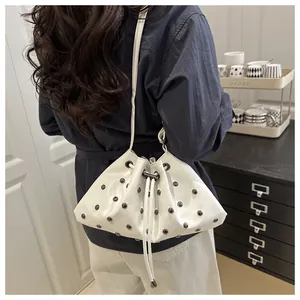 Dettaglio della borsa a secchiello in pelle bianca con borchie metalliche su una modella