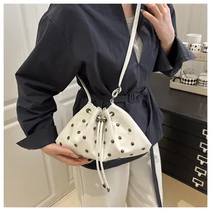 Dettaglio borsa a secchiello bianca con coulisse e borchie argentate su sfondo blu scuro