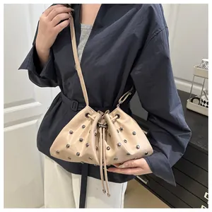 Dettaglio di una borsa a secchiello beige con coulisse e rivetti in argento e tracolla