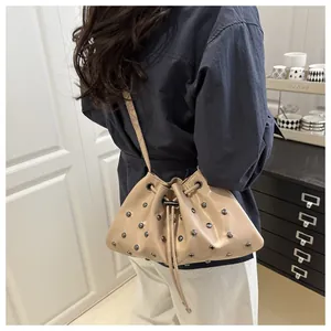 Dettaglio borsa a secchiello beige con coulisse e borchie argento indossata a tracolla