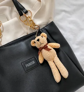 Detail shot of a plush brown bear charm with a satin bow on a black tote bag