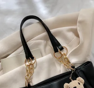 Detail of black leather tote bag with gold chain strap and teddy bear charm accessory