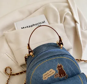 Detalle de bolso vaquero azul con ilustración de gato y asa de mano redonda café