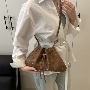 Borsa a secchiello marrone con borchie e coulisse portata a spalla da donna