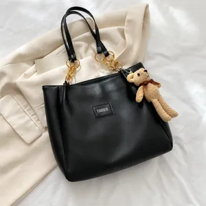 Detail of black leather tote bag featuring gold chain strap and cute bear charm accent