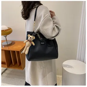 Detail of black matte leather tote bag with gold chain strap and yellow bear charm