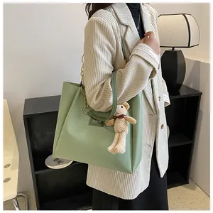 Detail of sage green tote bag featuring chain strap and cute beige bear pendant