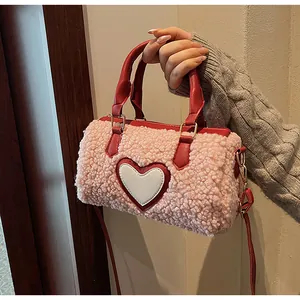Détail du sac boston rose en peluche avec poignées en cuir rouge et écusson cœur