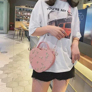 Pink heart-shaped crossbody bag with floral embroidery and gold chain strap on a model