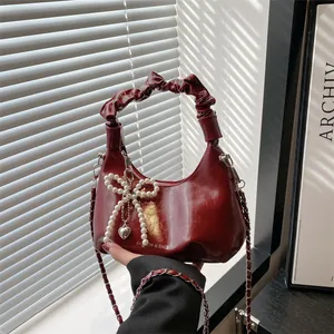 Dark red pleated leather handbag with pearl bow charm and chain strap in soft window light