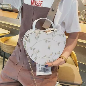 White heart-shaped handbag with floral embroidery and gold chain strap on model