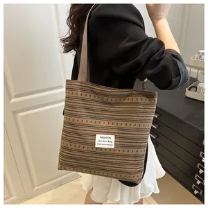 Gros plan du sac cabas en toile rayée marron avec étiquette tissée sur blazer noir