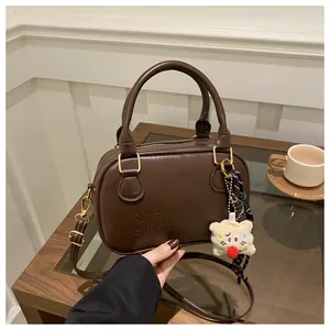 Vue détaillée du sac bowling marron foncé avec ferrures dorées et breloque petit ours