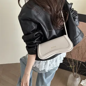 Minimalist cream-colored saddle shoulder bag with gold lettering shown on a model