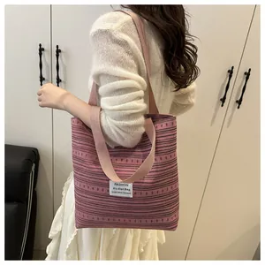 Détail d'un sac cabas en toile à rayures roses avec bandoulière tissée et logo frontal
