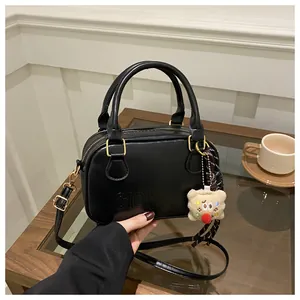 Détail d'un sac bowling vintage en cuir noir avec ferrures dorées et breloque ours en peluche