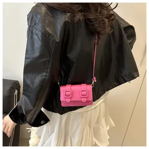 Dettaglio mini borsa a tracolla rosa acceso con doppie fibbie su sfondo di abiti scuri