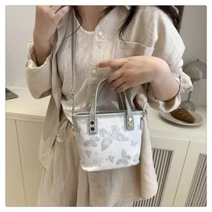 Détail du sac à bandoulière blanc avec imprimé papillon et fine sangle en cuir gris