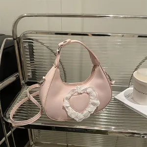 Borsa rosa a mezzaluna con cuore in pizzo da donna su un ripiano in vetro