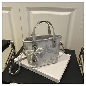Détail du sac cabas argenté avec imprimé papillon, nœud en perles et breloque cœur