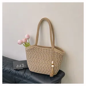Detail of hand-woven straw shoulder bag with black stripes and decorative tassel charm